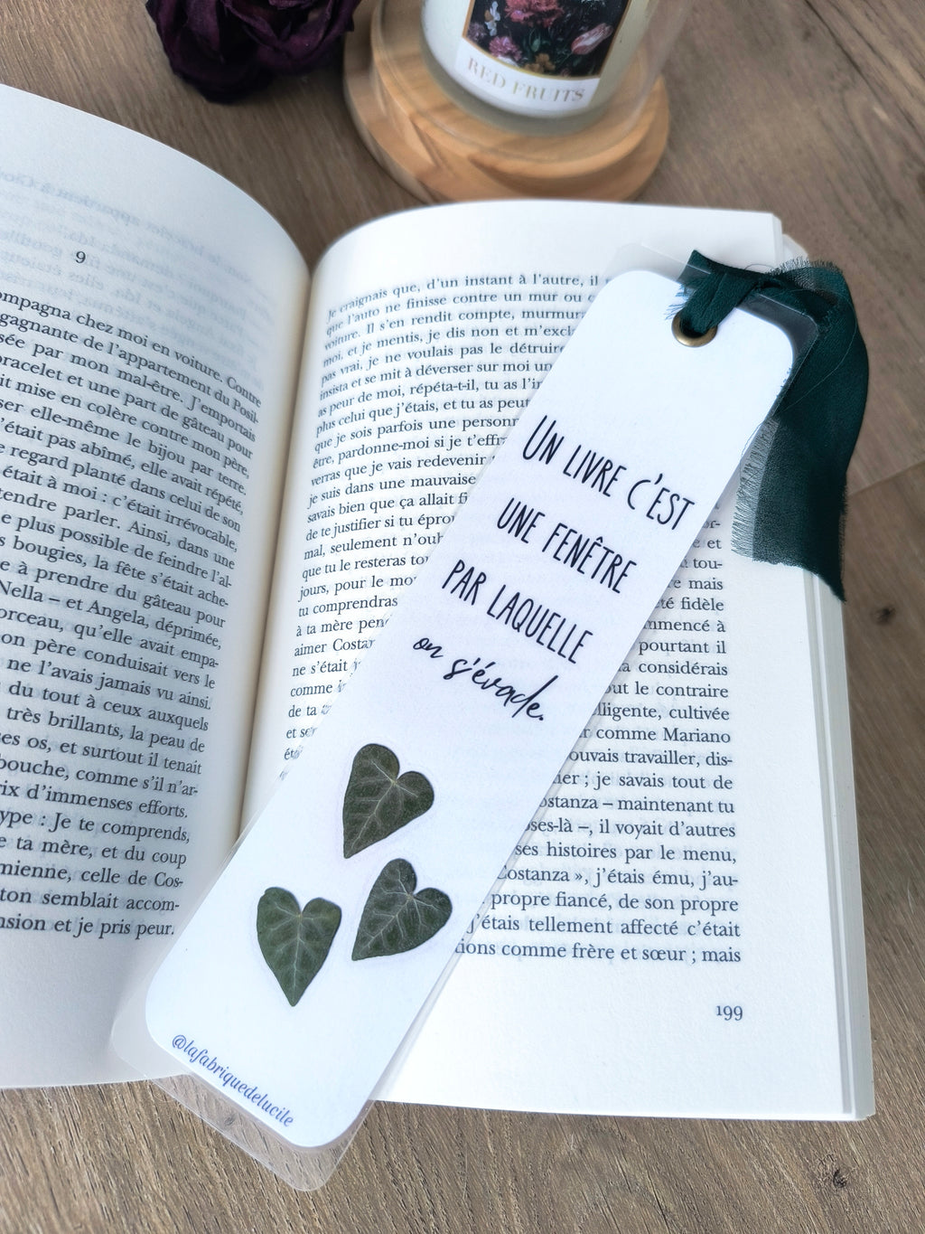 Marque-page en papier avec feuilles vertes en forme de cœur et citation 'Un livre c'est une fenêtre par laquelle on s'évade', posé sur un livre ouvert.